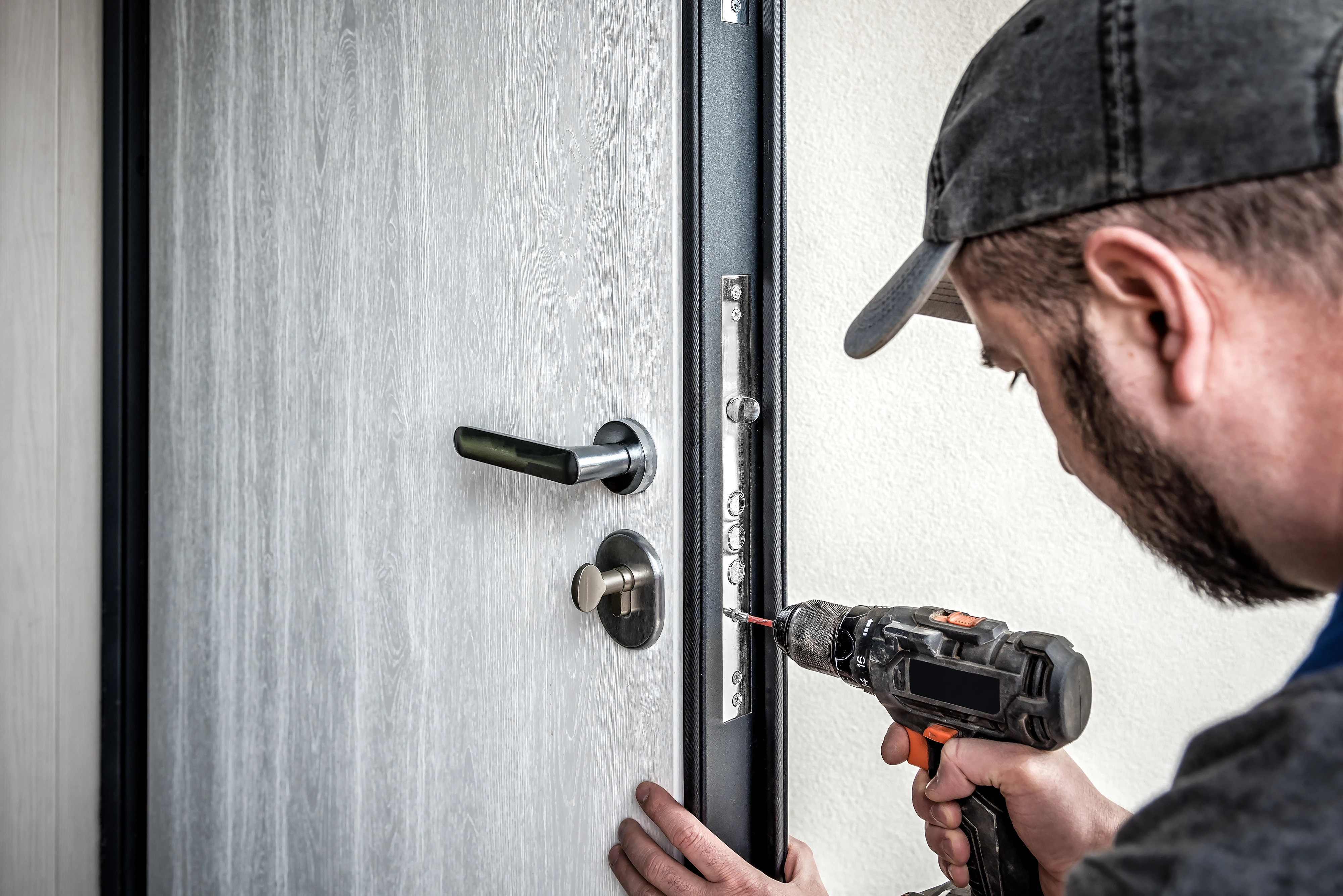 A person is using a power drill to install a door lock on a modern door.